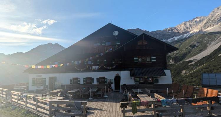 Refuge de montagne isolé avec drapeaux de prière dans la lumière du soir contre des pentes alpines escarpées.
