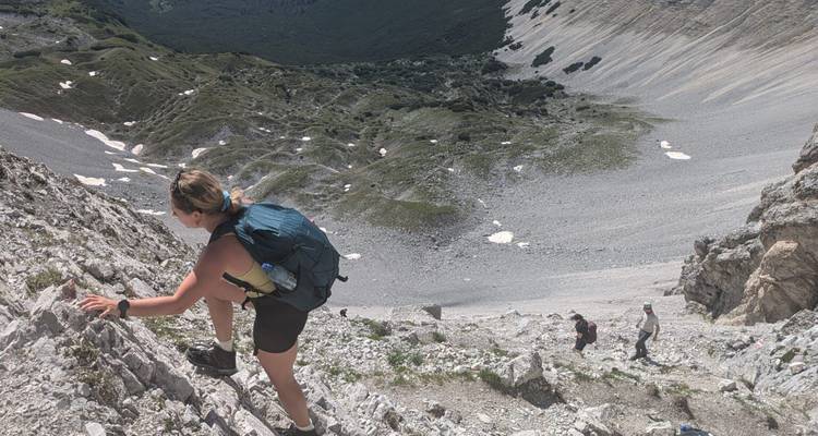 Randonneuse grimpant sur une pente rocheuse escarpée tandis que ses compagnons suivent en contrebas.