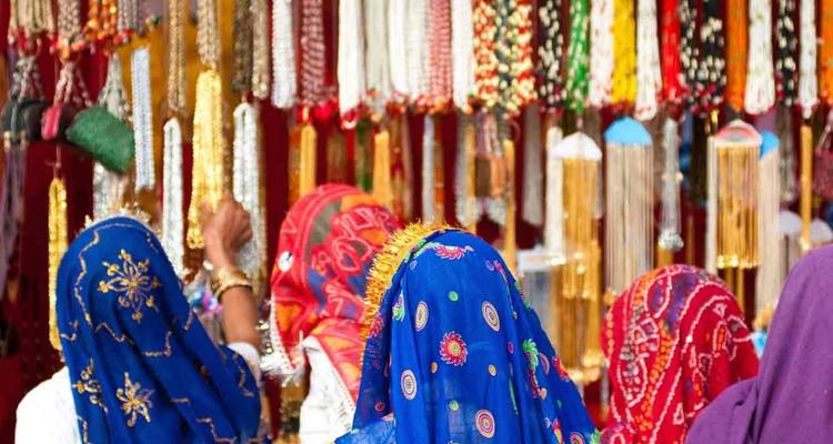 Vrouwen in kleurrijke traditionele kleding die hangende decoraties bekijken op een markt.