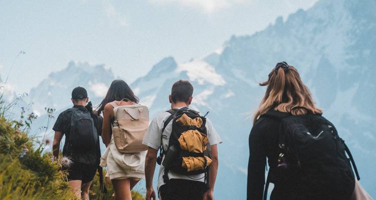 Grupo de excursionistas ascendiendo por una cresta cubierta de hierba con dramáticas montañas nevadas de fondo.