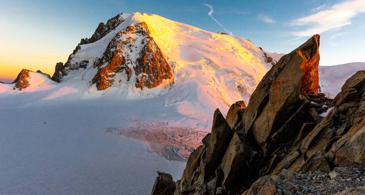 La luz del amanecer pinta un pico cubierto de nieve y rocas escarpadas sobre una vasta extensión helada.