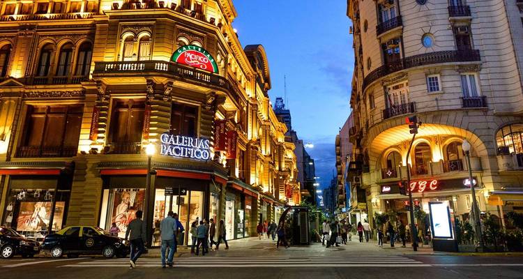 Una animada escena callejera en Buenos Aires con personas caminando frente a edificios iluminados.