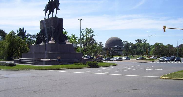 Una vista de la calle con una estatua y una estructura de cúpula al fondo.