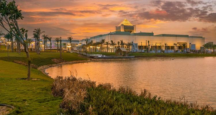 Une vue au coucher du soleil d'un bâtiment avec un lac et des palmiers.