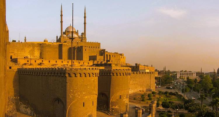 Une vue d'une citadelle ancienne avec une mosquée dans une lumière dorée chaleureuse.