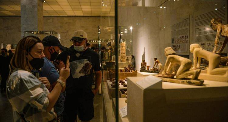 Des visiteurs observant des artefacts anciens dans un musée faiblement éclairé.