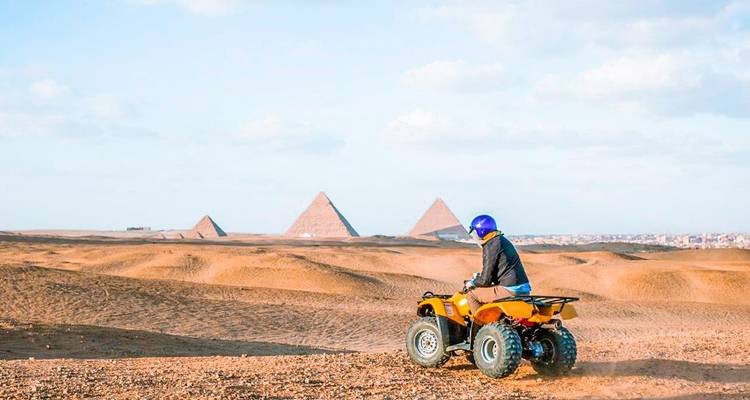 Une personne conduisant un VTT dans un paysage désertique avec des pyramides au loin.