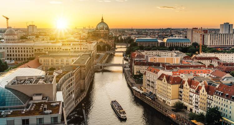 Sol poniéndose sobre la catedral de Berlín y el río Spree con un barco turístico navegando abajo.