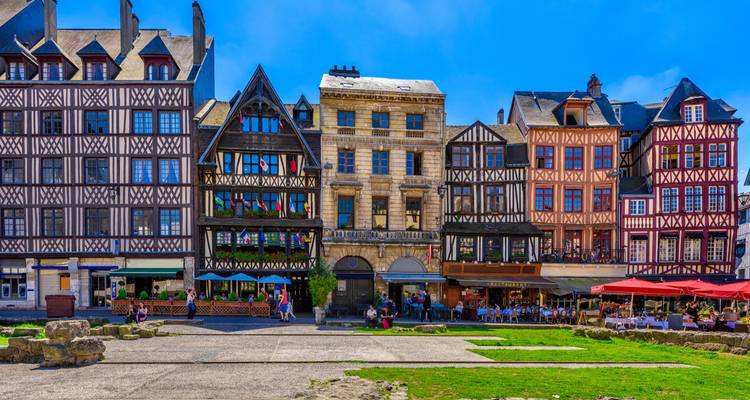 Maisons médiévales à colombages entourant une place ensoleillée à Rouen, France avec des gens qui se détendent en plein air.