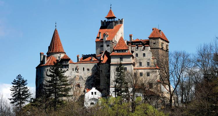 Le château de Bran avec ses toits rouges and ses tours s'élève au-dessus des collines boisées de Transylvanie.