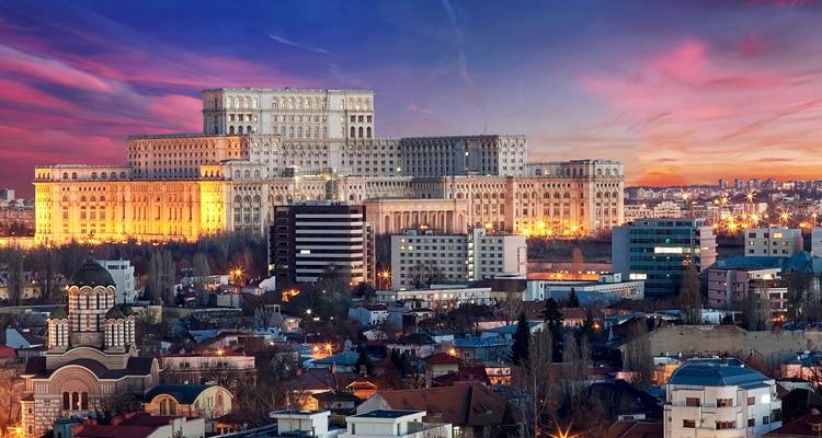 Evening lights illuminate Bucharest’s Palace of Parliament towering over surrounding rooftops.