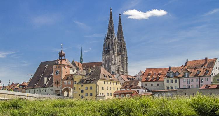 Historische skyline van Regensburg met zijn kathedraal met dubbele torens en middeleeuwse gebouwen onder een levendige blauwe hemel.
