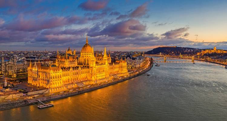 Aerial dusk view of Budapest Parliament lit golden beside the Danube River with Chain Bridge and city lights