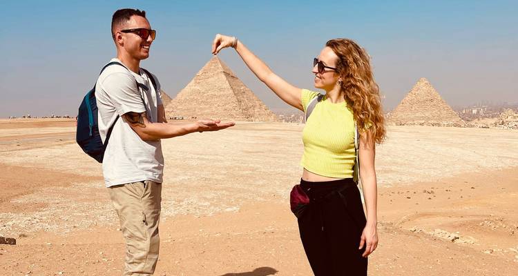 Couple posant de manière ludique avec une perspective forcée des pyramides dans le désert de Gizeh.