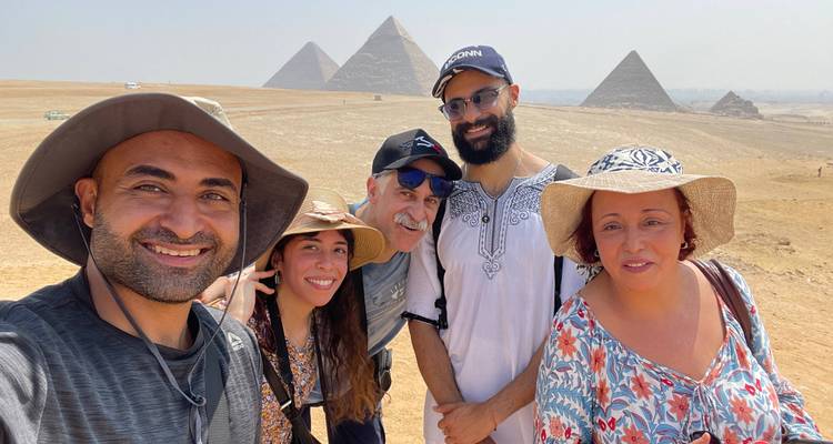 Guide touristique et voyageurs posant avec plusieurs pyramides derrière eux par une journée brumeuse.