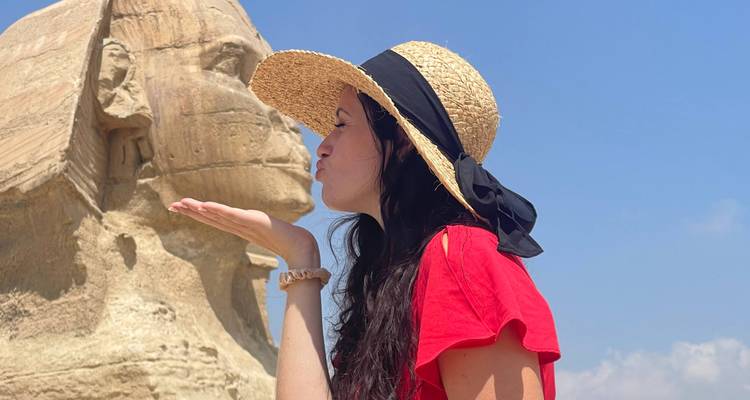 Femme faisant semblant de manière ludique d'embrasser la statue du Sphinx à Gizeh sous un ciel bleu.