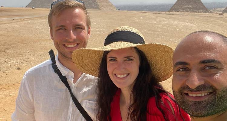 Selfie de trois amis souriants avec les pyramides et le désert qui s'étendent derrière.