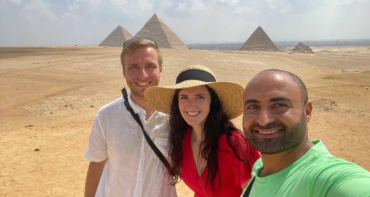 Deux touristes et leur guide sourient avec les pyramides de Gizeh qui s'étendent en arrière-plan.