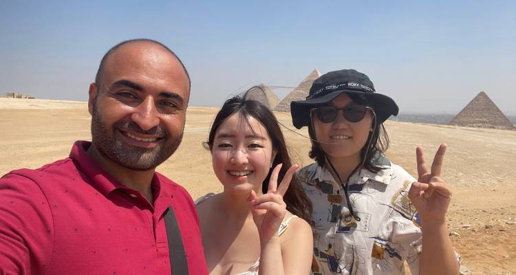 Trois jeunes voyageurs font des signes de paix avec les pyramides derrière eux par une journée ensoleillée.