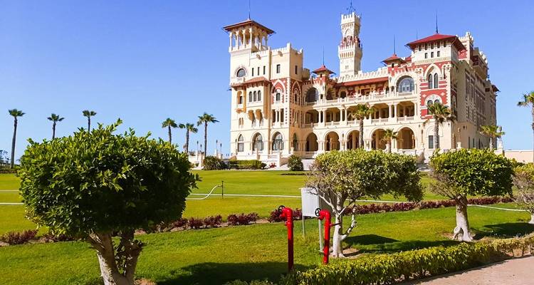 Élégant palais Montaza avec des pelouses soignées et des palmiers sous un ciel clair.