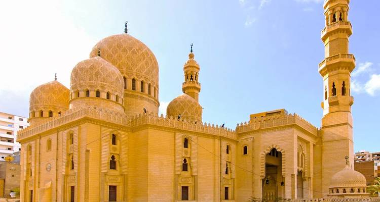 Mosquée en pierre dorée avec des dômes ornés et un minaret élancé qui scintille sous la lumière éclatante du jour.
