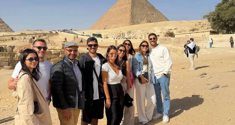Groupe de voyageurs pose devant une pyramide avec des touristes éparpillés en arrière-plan.