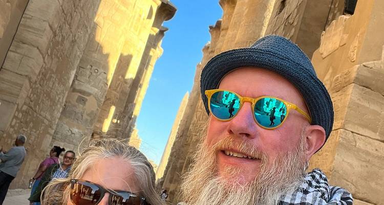 Selfie d'un couple portant des lunettes de soleil réfléchissantes parmi les imposantes colonnes de grès de Louxor.