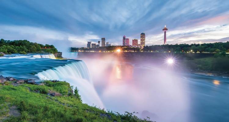 Langzeitbelichtungsaufnahme der Niagarafälle in der Dämmerung mit in Nebel leuchtenden Stadtlichtern.