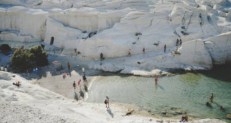 Formaciones rocosas blancas similares a la luna de la playa Sarakiniko con una piscina natural donde los nadadores disfrutan del agua cristalina.