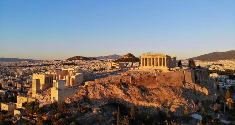 Vista panorámica aérea de la hora dorada de la colina de la Acrópolis dominando Atenas con montañas al fondo.