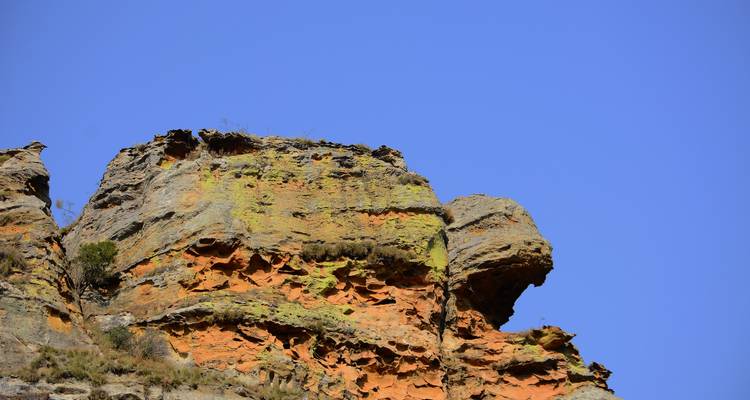 Falaise rocheuse déchiquetée tachée de lichens orange et jaunes s'élançant dans un ciel bleu sans nuages.