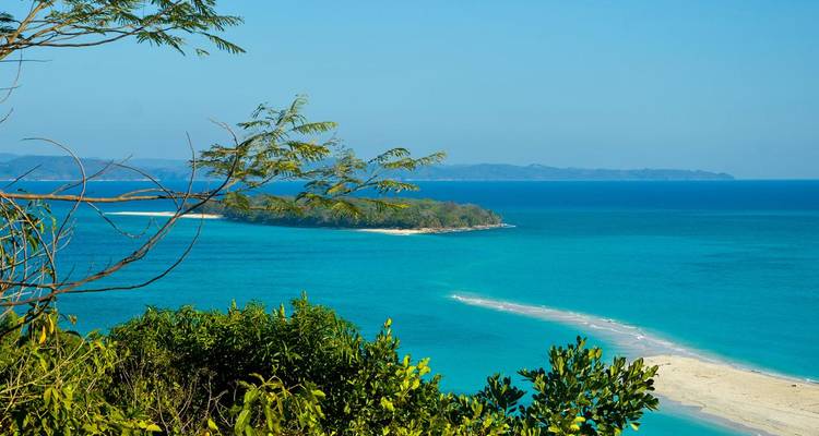 Baie d'un bleu éclatant avec un étroit cordon de sable blanc reliant une île boisée au continent.