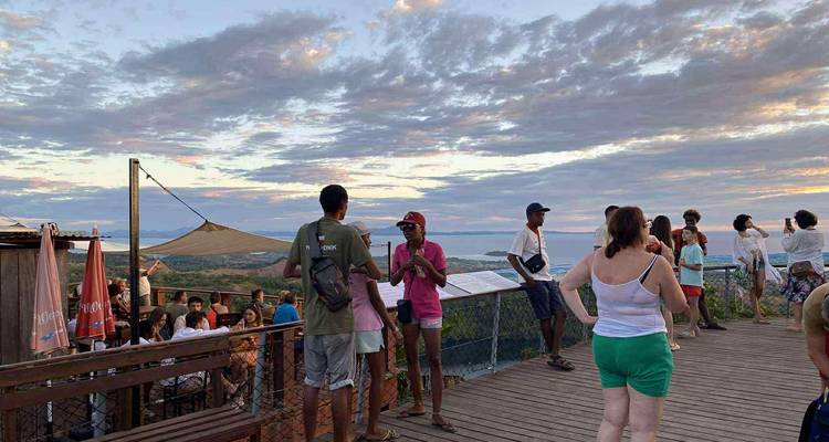 Les visiteurs se mélangent sur une plateforme d'observation en bois surplombant l'océan et les nuages éclairés par le coucher de soleil.