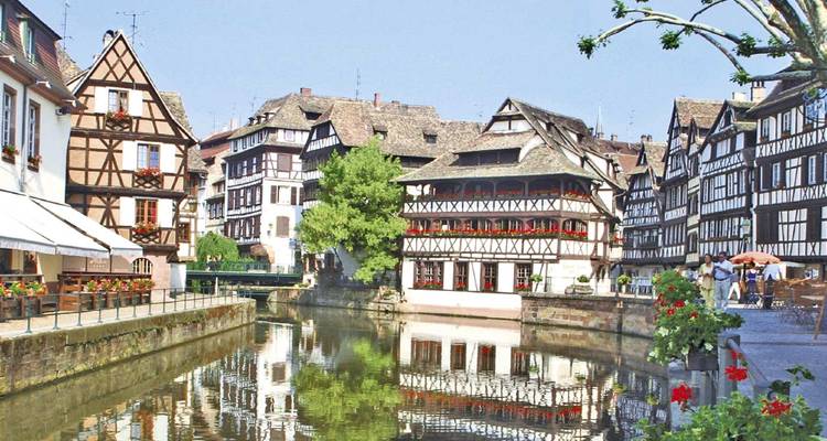 Encantadoras casas de entramado de madera reflejadas en un canal tranquilo en el distrito Petite France de Estrasburgo adornadas con flores.