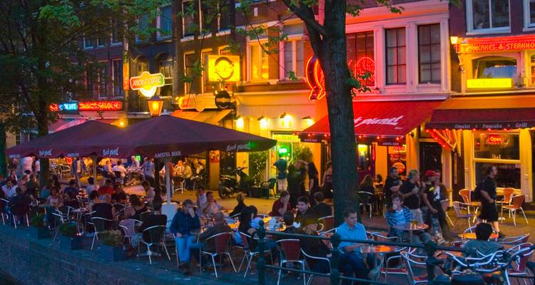 Scène du soir sur un canal d'Amsterdam bordé de cafés animés et d'enseignes au néon.