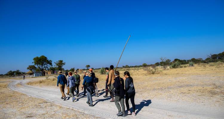 Grupo de excursionistas siguiendo a un guía local a través de un sendero arenoso en un paisaje seco y abierto bajo un cielo azul despejado.