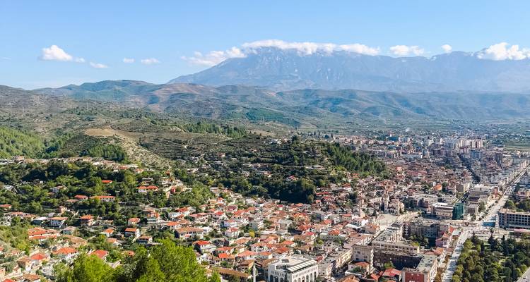 Aerial panorama of Tirana sprawling between green hills with distant mountain range.
