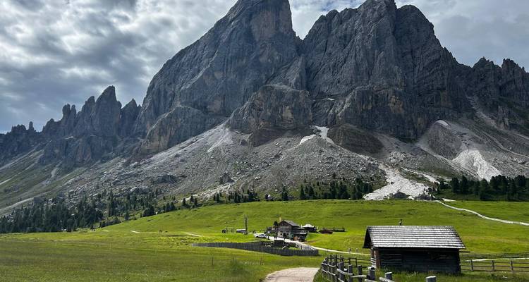 Les pics acérés des Dolomites s'élèvent au-dessus des prairies alpines et d'un chalet rustique.