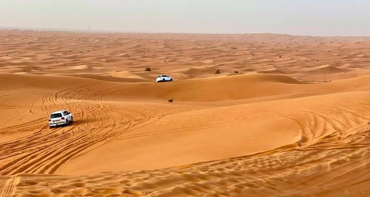 Vast orange sand dunes with two off-road vehicles carving tracks across the Sahara.