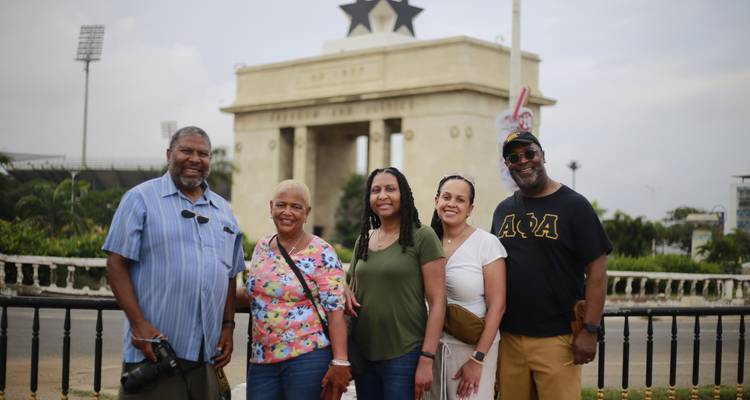 Petit groupe de voyageurs sourit devant la Porte de l'Étoile Noire d'Accra et le terrain de parade.