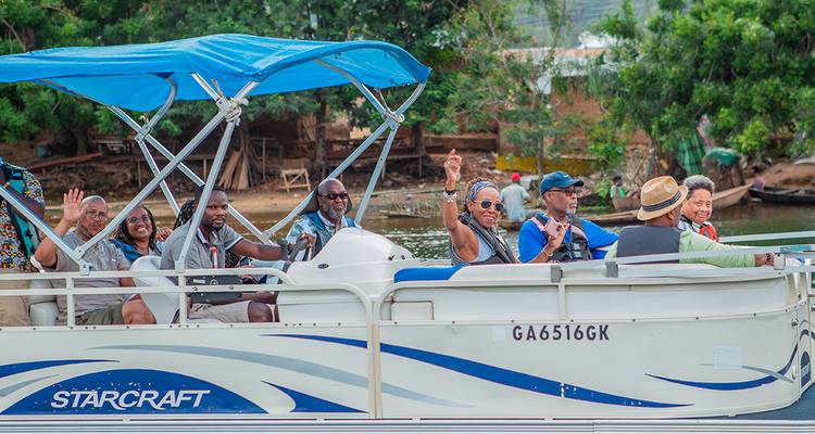 Des touristes font signe depuis un bateau à fond plat avec un auvent bleu naviguant le long d'une rivière calme.