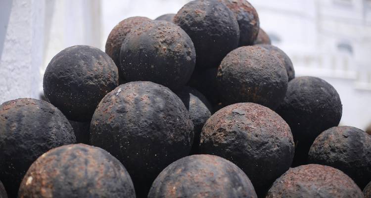 Boulets de canon en fer rouillé empilés en pyramide contre les murs blancs d'une forteresse côtière.
