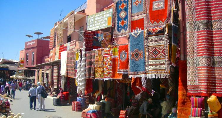 Vibrant Marrakesh market street lined with hanging Berber rugs and bustling shoppers.