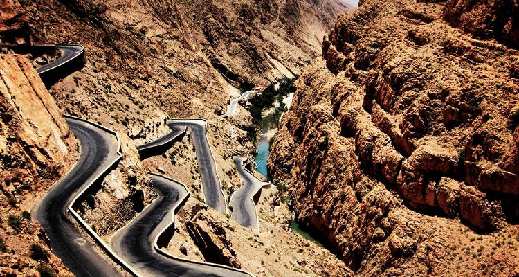 Serpentine mountain road winding through rugged reddish gorge cliffs.