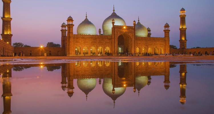 Badshahi Mosque illuminated at twilight reflecting perfectly in still water