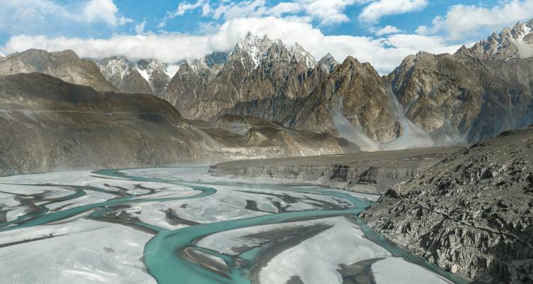 Dramatic braided turquoise river winding through barren valley beneath jagged snow-capped peaks