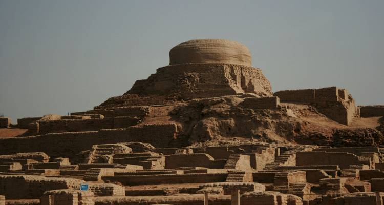 Ancient brick stupa rising above excavated ruins of an Indus Valley civilisation site under hazy sky