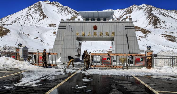 Snow-covered Khunjerab Pass border gate with soldiers standing amid melting slush