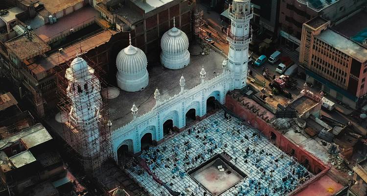 Aerial view of ornate white domed mosque amidst dense urban landscape under construction scaffolding