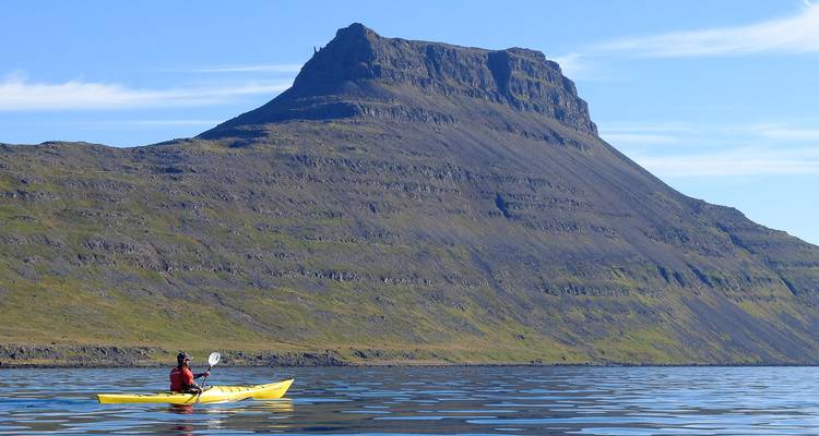 Sea kayaker paddling in calm Icelandic fjord beneath a steep table mountain